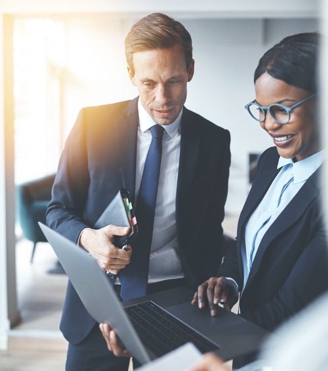 Well dressed woman holds a laptop and well dressed man looks at the laptop