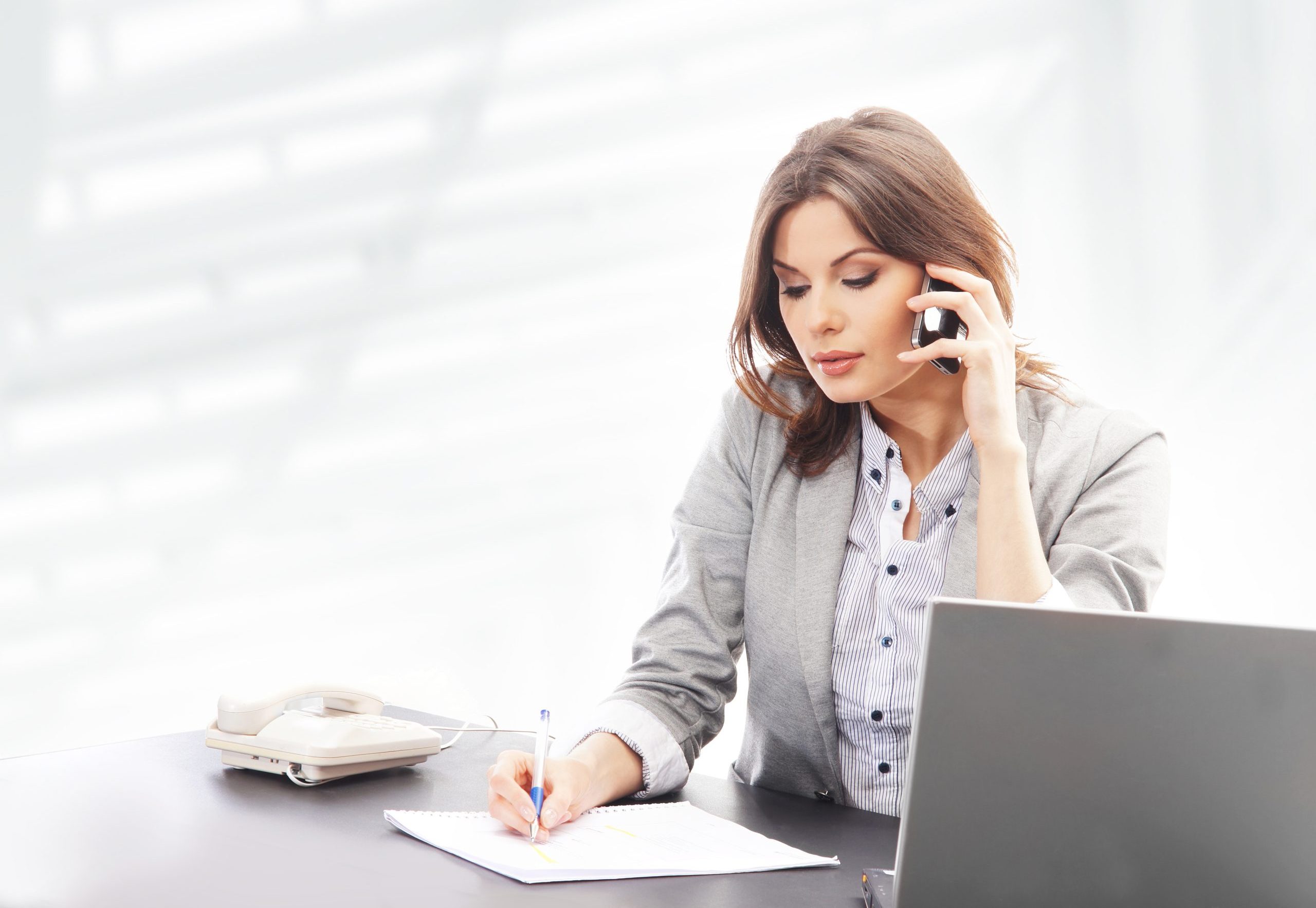 A well dressed woman on the phone while making notes