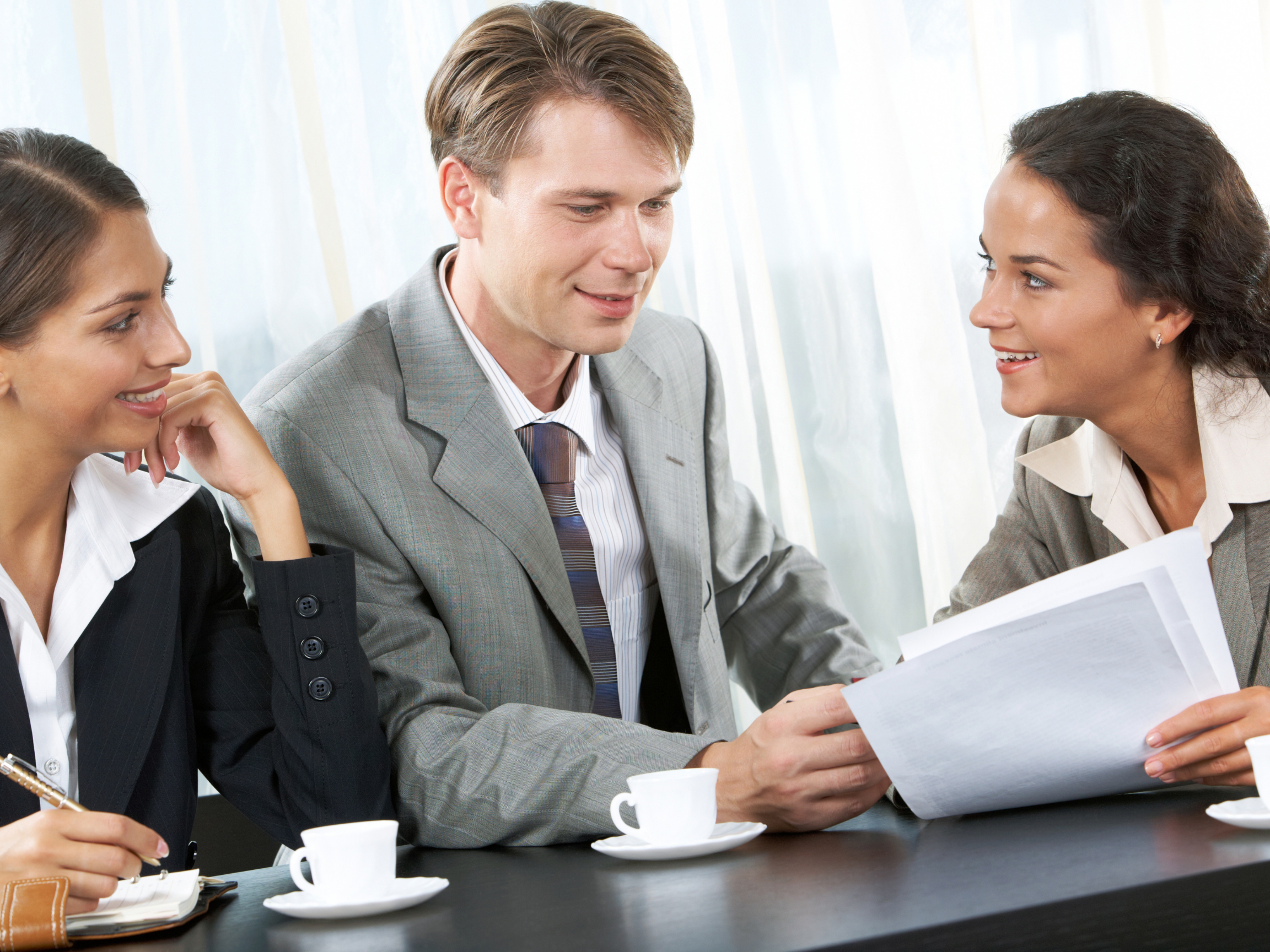 Three well dressed people talking to each other. One woman holds some sheets of paper